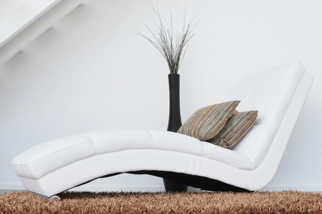 Na zdjęciu wazon i minimalistyczny leżak / fotel.